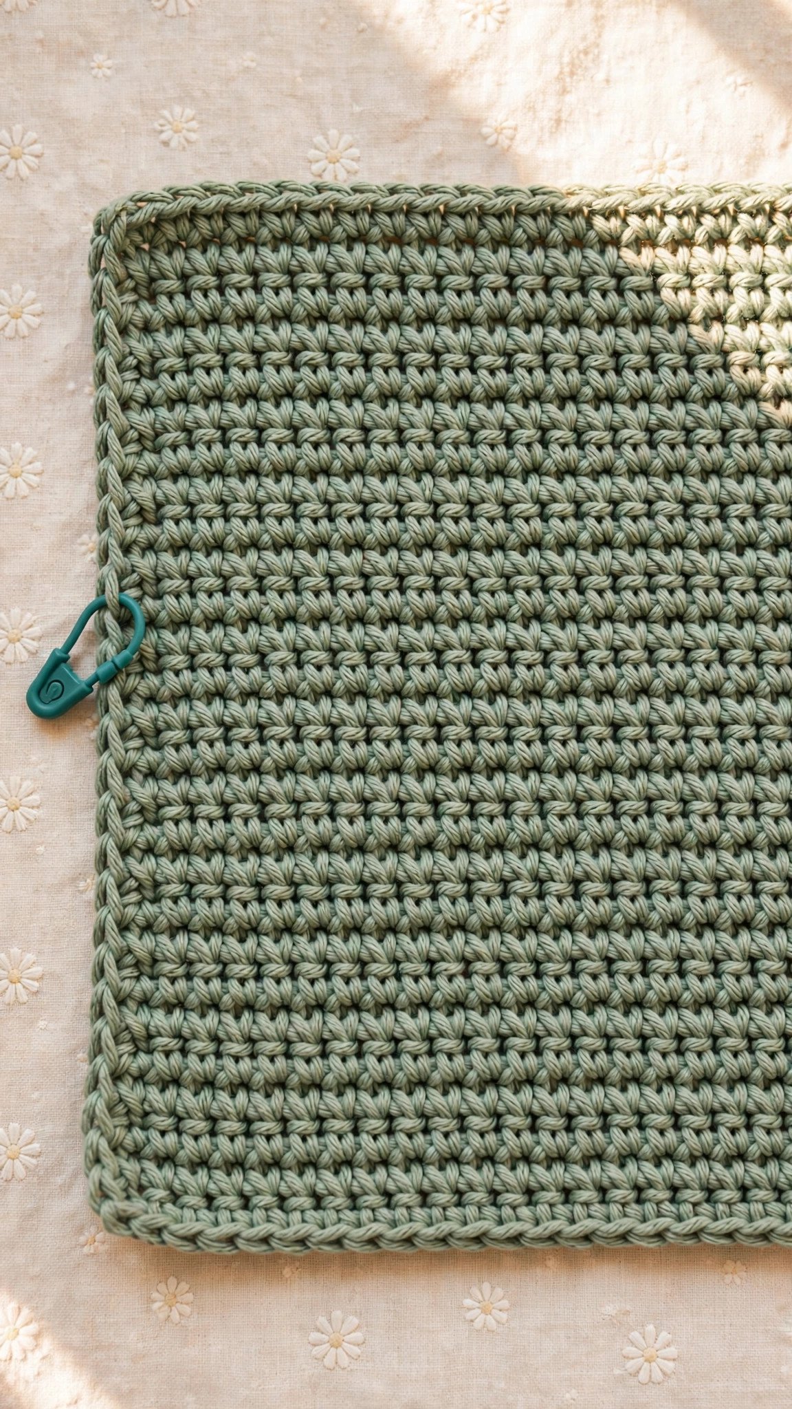 Neat rows of sage single crochet with a teal stitch marker on the edge stitch